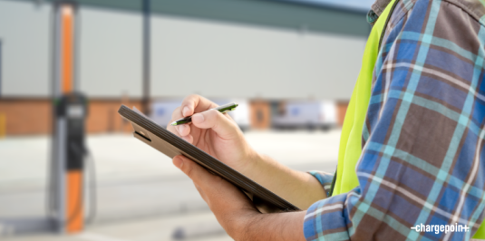 Person holding an ipad and writing on it and ChargePoint CP6000 in a distant view