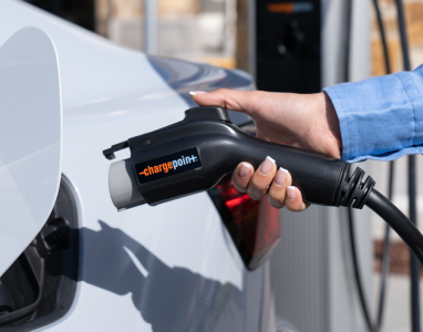 Hand plugging a ChargePoint connector into a white electric car.