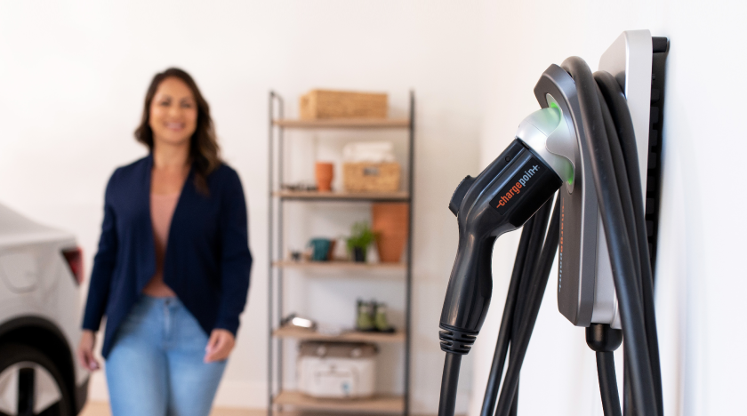 A woman stands in a room with a "ChargePoint" electric vehicle charger in focus.