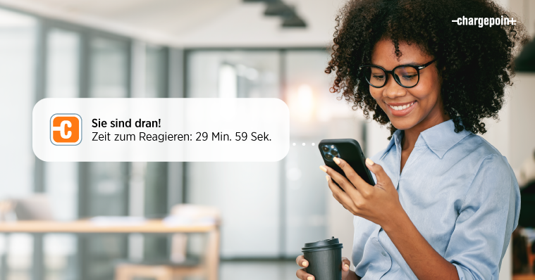 Eine Person, die auf ihr Handy schaut und lächelt, während sie eine ChargePoint‑Wartelistenbenachrichtigung erhält.