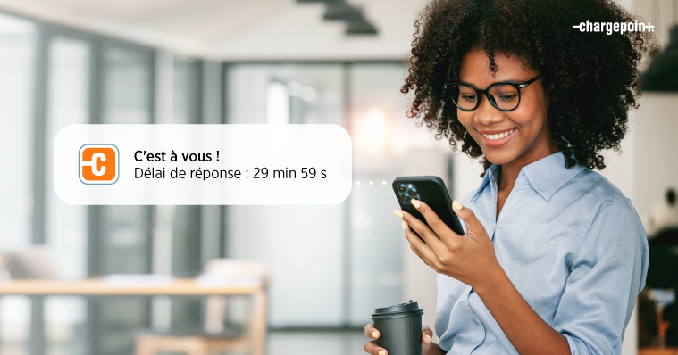 Une personne regardant son téléphone avec un visage souriant en recevant une notification de la liste d’attente ChargePoint.