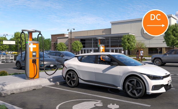 White electric car charging at a ChargePoint station, with a shopping center in the background.