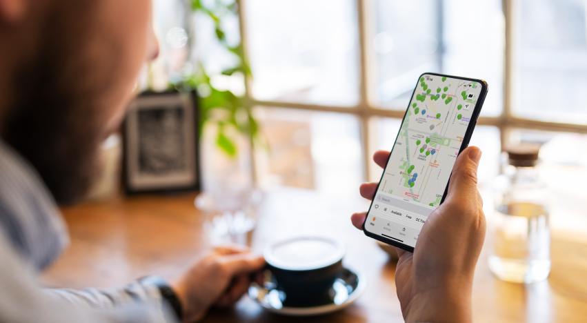 Close-up of a person's hand holding a smartphone showing a map of ChargePoint stations, with a cup of coffee in the foreground.